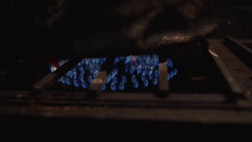 A close-up of a blue gas flame burning under a pot on a stove in the dark