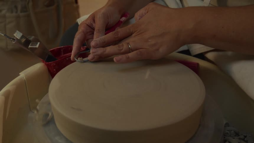 A potter uses a trimming tool to meticulously shape the base of a clay piece on a spinning pottery wheel in a studio