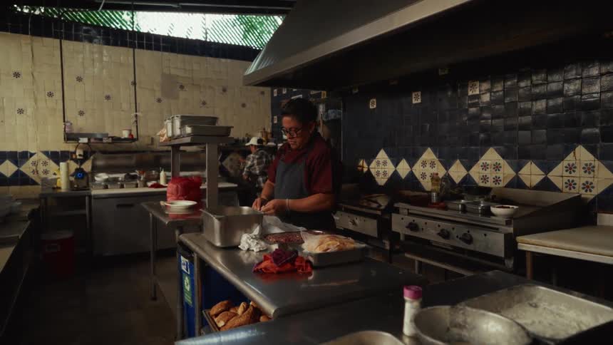 A chef with glasses works at a prep station in a commercial kitchen with traditional blue and white tile walls