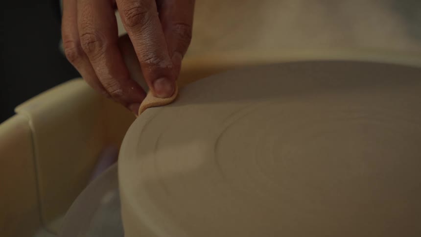 A potter uses a wooden rib tool to smooth the rim of a clay plate on a spinning pottery wheel