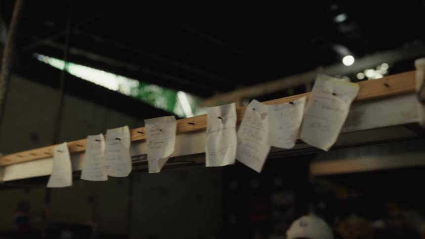 Handwritten food orders are pinned to a ticket rail in a busy restaurant kitchen