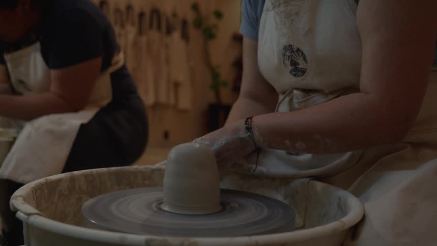 Slow motion close-up of a woman's hands expertly shaping wet clay on a spinning pottery wheel in a studio