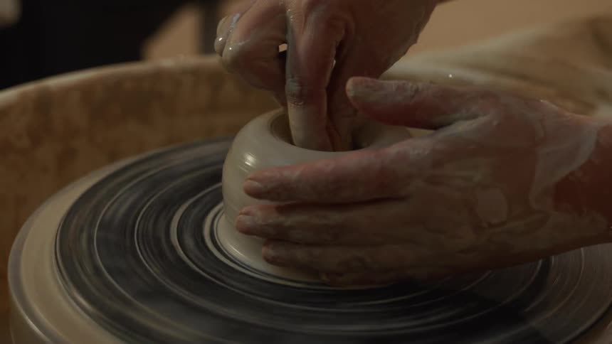 A potter's hands carefully shape and smooth the inside of a spinning clay pot with a sponge in a slow-motion close-up