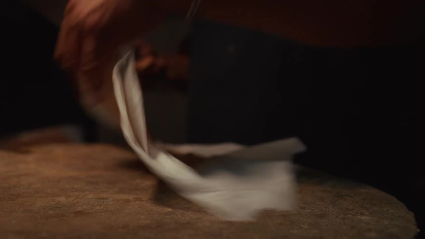 A professional chef in a dim kitchen expertly pounds a piece of meat with a mallet to tenderize it