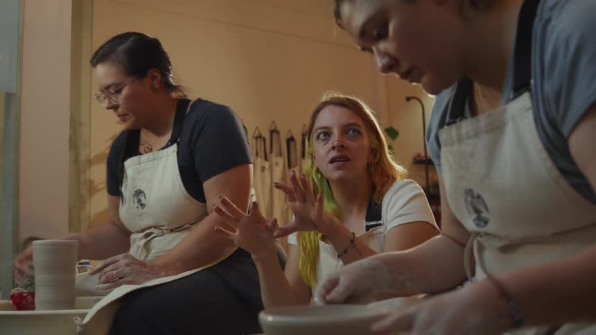 Three women in a pottery class learn to shape clay on the wheel in a creative studio environment
