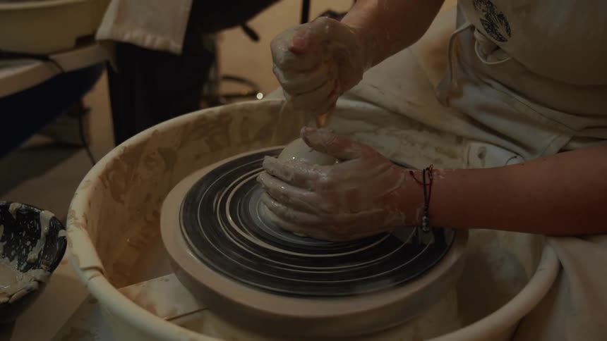 Close up of a potter's hands using a sponge to center and shape clay on a spinning pottery wheel