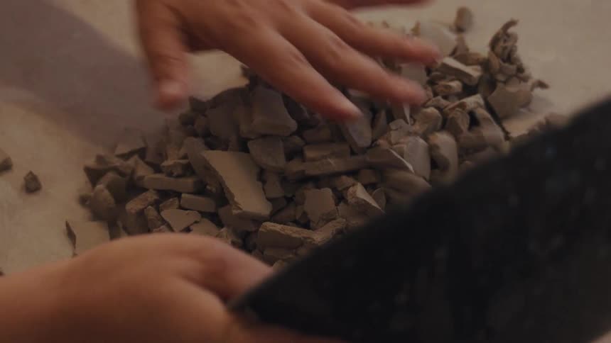 A ceramicist pours broken pieces of dry clay from a bowl onto a canvas surface in slow motion