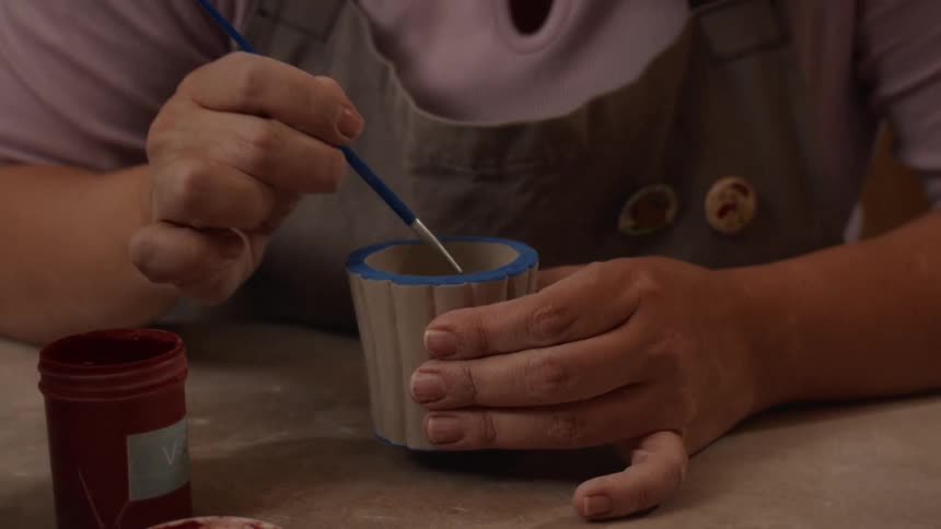 Close-up of an artisan's hands carefully painting the inside of a small ceramic cup with red paint in a pottery workshop