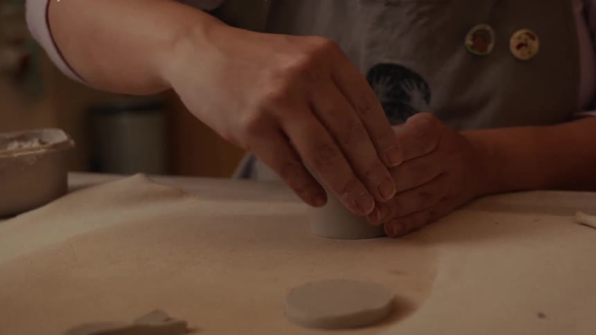 A ceramic artist carefully smooths and shapes a small, handmade clay cup in their workshop