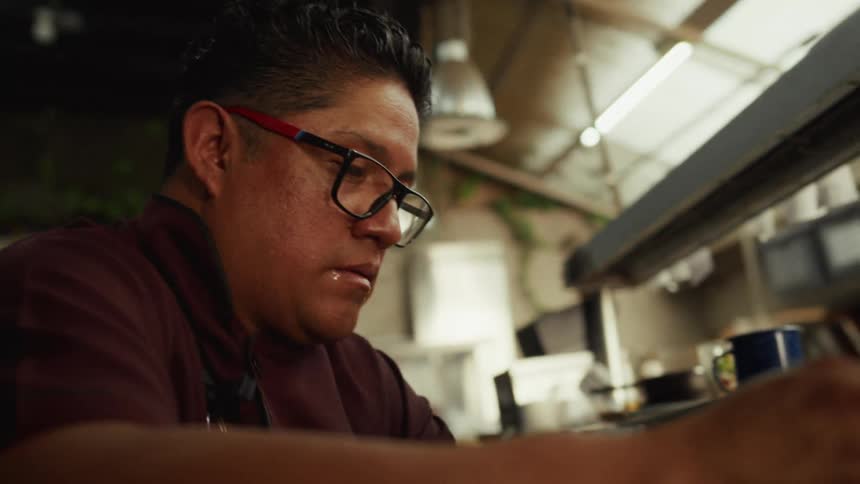 A focused chef wearing glasses meticulously works at his station in a professional restaurant kitchen