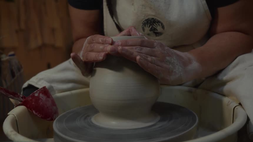 A potter's hands carefully shape and mold a piece of clay into a vase on a spinning pottery wheel in a studio