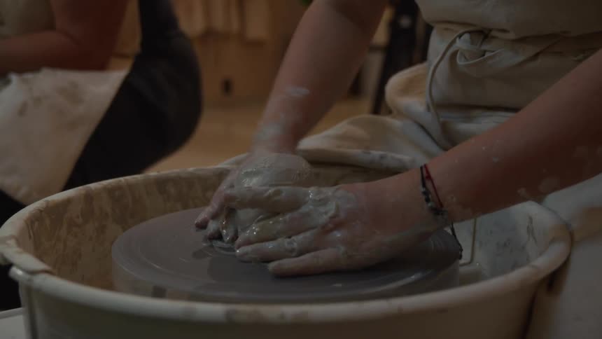 Close-up of an artisan's hands centering a ball of wet clay on a spinning pottery wheel