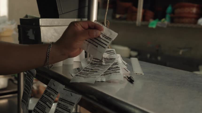 A chef grabs a new printed order ticket from the printer and places it on the ticket spike in a busy restaurant kitchen
