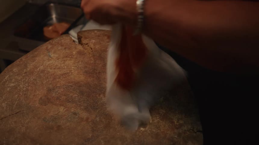 A chef pounds a raw chicken breast thin with a meat tenderizer on a rustic wooden cutting board