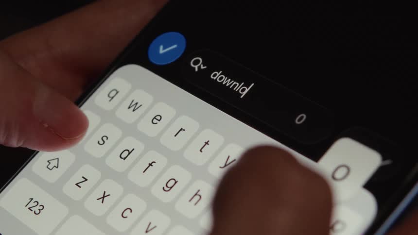 A person types the word 'download' into a search bar on a smartphone with a dark mode interface