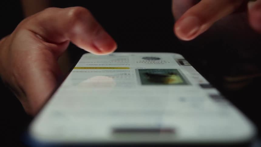 A close-up shot of fingers scrolling and tapping on a brightly lit smartphone screen while browsing an online store in a dark environment
