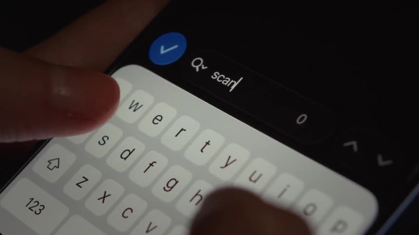 A close-up shot of a person's fingers typing the word 'scan' into a search bar on a smartphone in dark mode