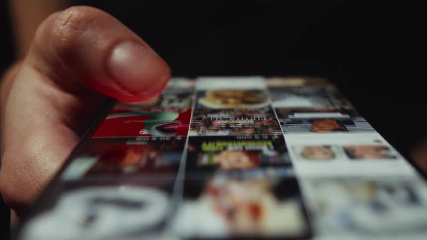 Macro close-up shot of a thumb scrolling through an image-based social media feed on a smartphone in a dark room