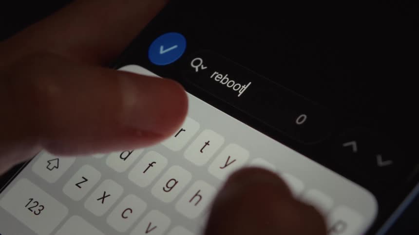 A close-up macro shot of fingers typing the word 'reboot' into a smartphone search bar