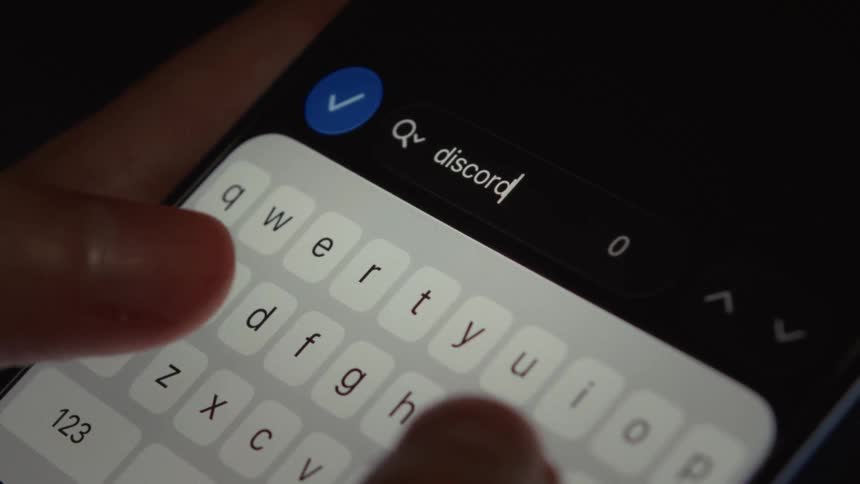 A close-up of fingers typing 'discord' into a search bar on a smartphone screen in dark mode