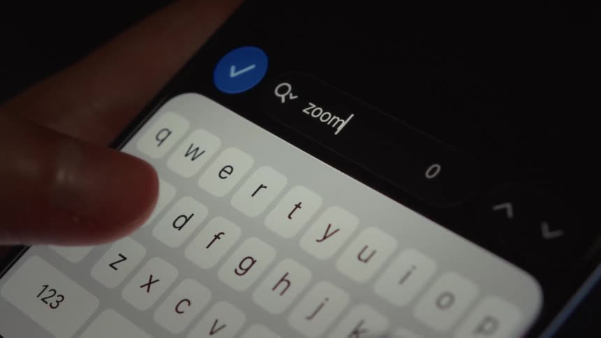 A macro shot shows fingers typing the word 'zoom' into a search bar on a smartphone
