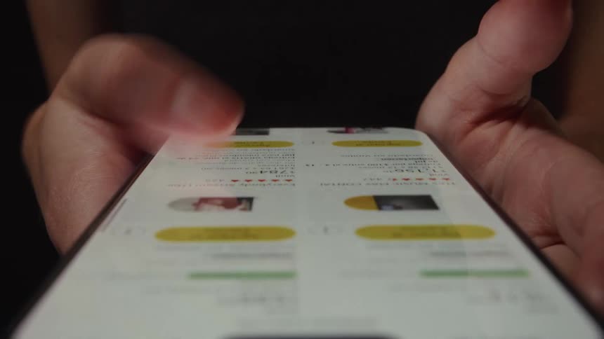 Macro view of hands scrolling through an online shopping app on a smartphone in a dark room