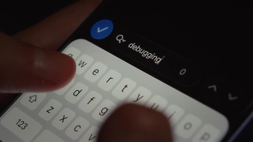 A user types the word 'debugging' into a search bar on a smartphone screen in dark mode