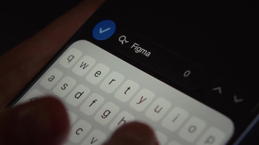 A close-up of a person typing the word 'Figma' into a search bar on a smartphone in a dark room