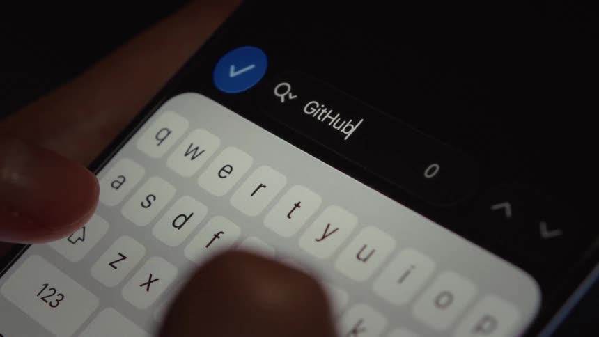 A macro close-up shot of a person typing 'GitHub' into a smartphone's search bar