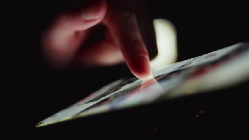 A dimly lit, cinematic close-up of a finger scrolling through a vibrant feed on a touchscreen device at night