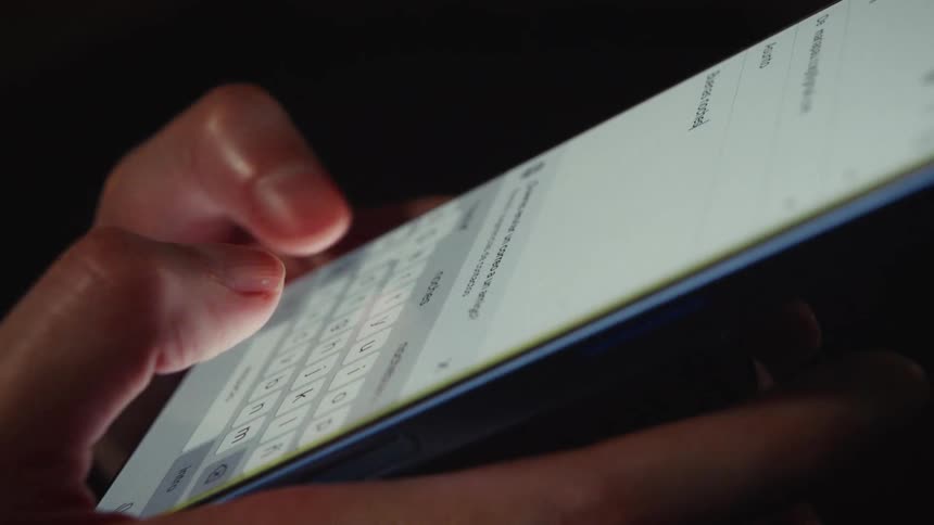 A close-up shot of a person's hands typing on a smartphone's touch screen in a dark room
