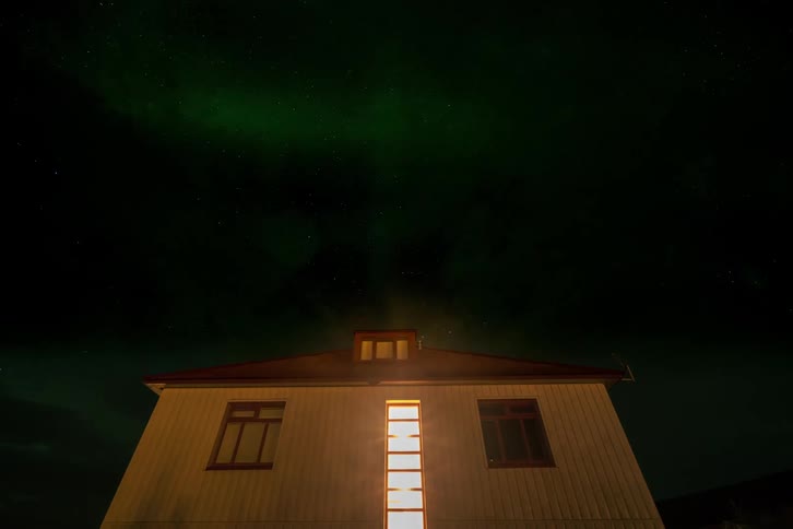 Time-lapse of green northern lights flashing over a house