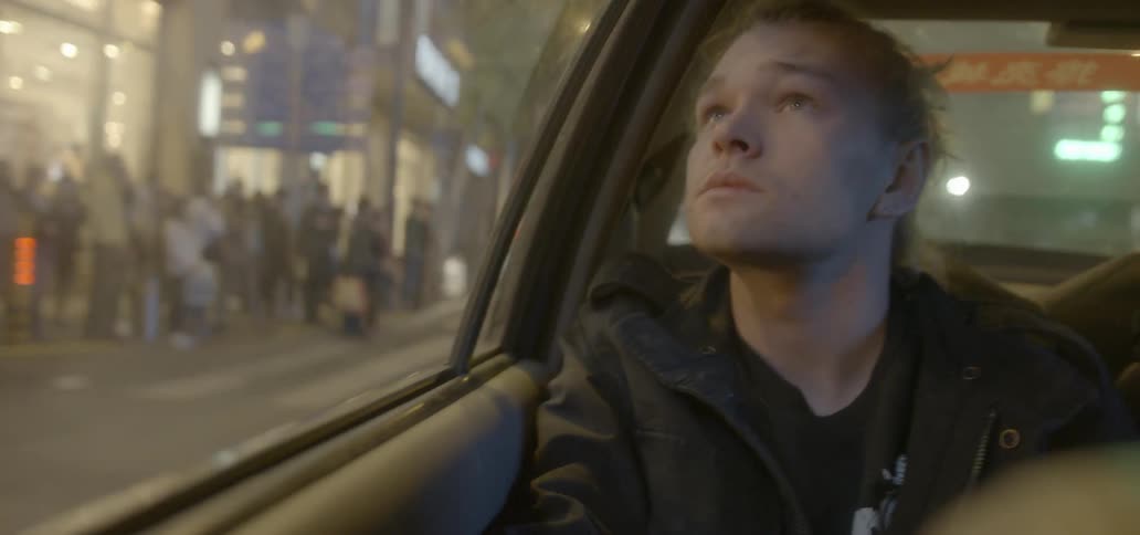 A man rides in a car and looks out the window at city buildings