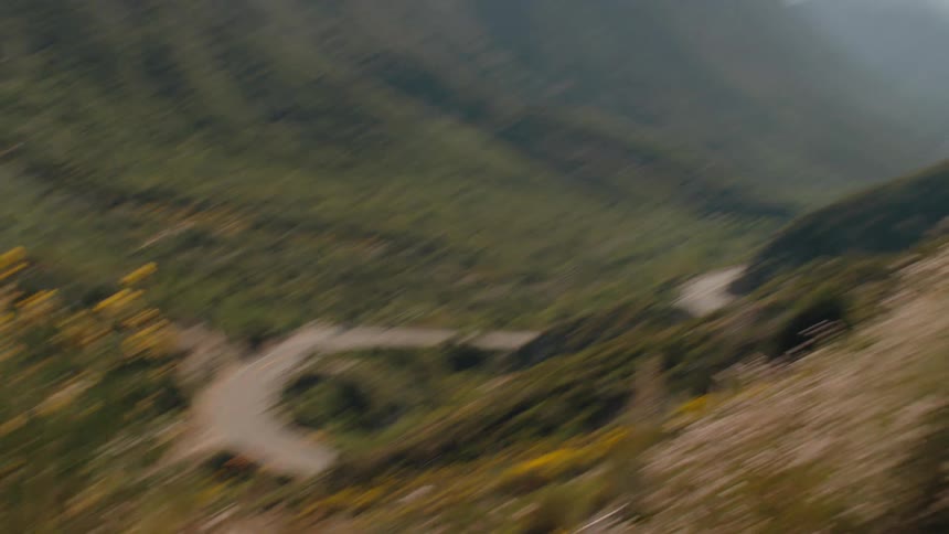 A cinematic zoom out from a curvy road reveals a sweeping vista of a green mountain valley