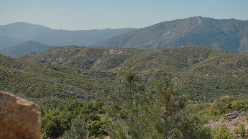 A sweeping view of a verdant mountain range under a clear, bright sky, with a slow zoom highlighting the vast landscape