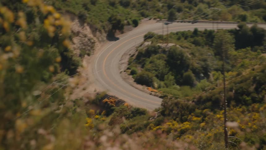 Scenic mountain vista tilts down with a whip zoom to an empty, curved road in a green canyon