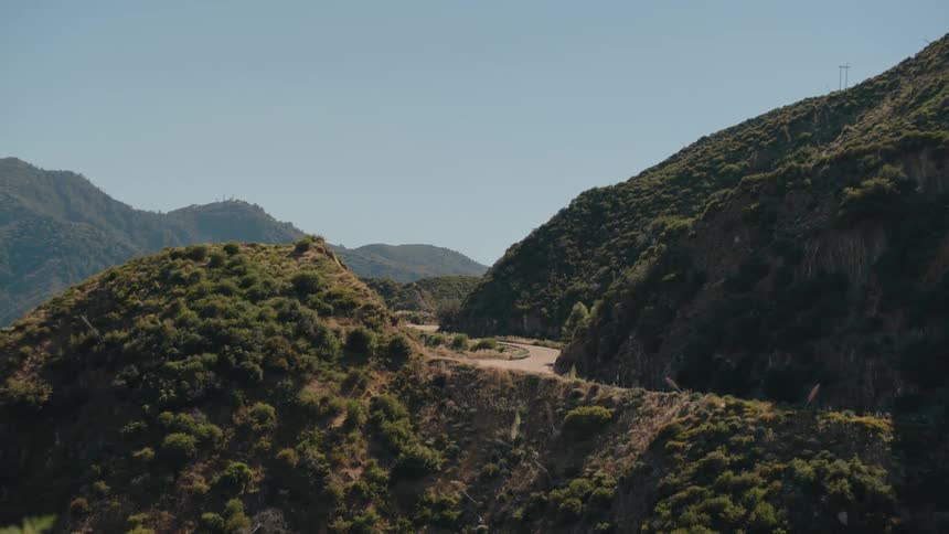 A scenic view of a winding road through a lush green mountain pass on a sunny day