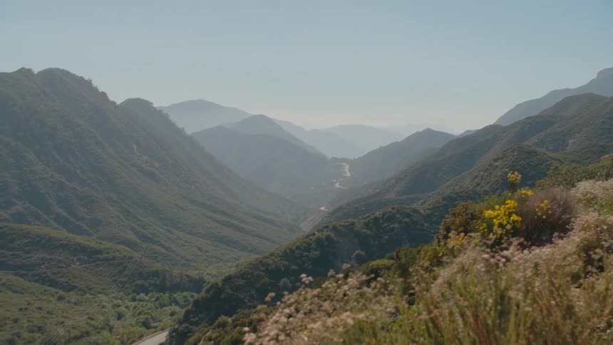 A sweeping panoramic view of a hazy mountain valley slowly zooms in to focus on a winding road below