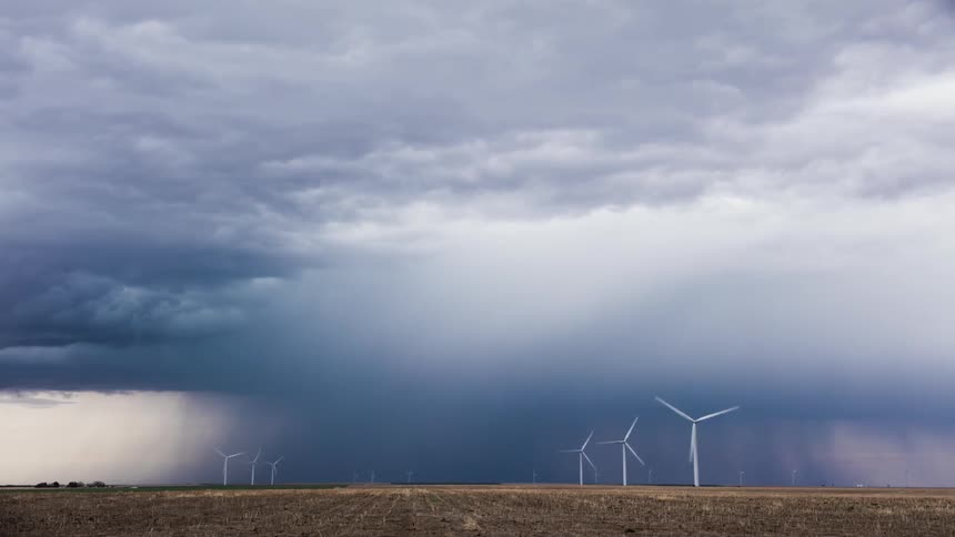 The windmills turn fast on the field as storm clouds pass