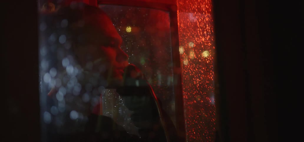 A man is talking on the phone in a booth at night