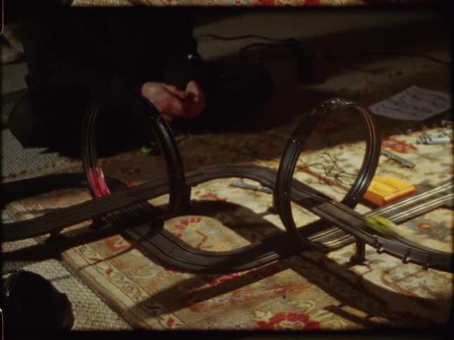 Vintage home movie footage shows two slot cars racing around a figure-eight track set up on a rug