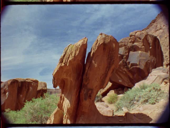 Vintage 8mm film of a unique, split red rock formation in a desert canyon under a blue sky