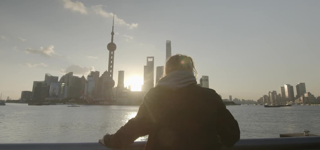 A man leans on a railing by the water looking at the city