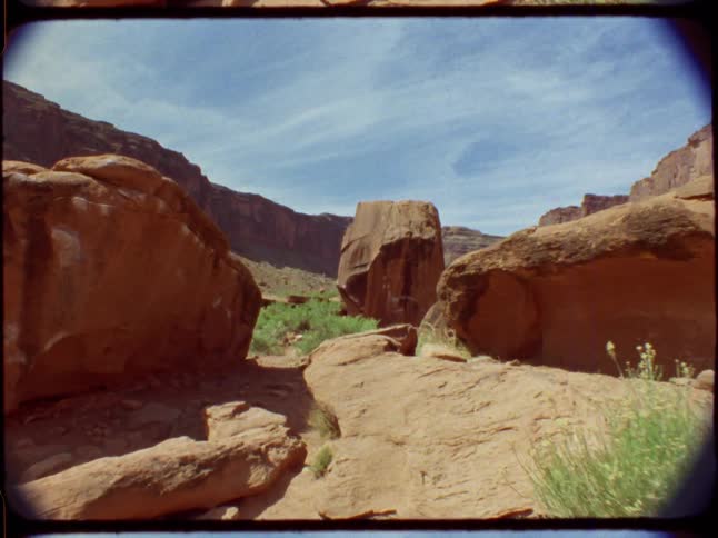 Vintage film footage captures a slow dolly shot moving through a vast desert canyon with red rock formations