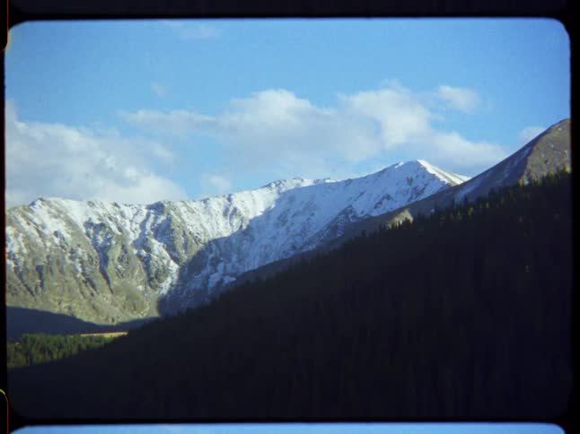 A beautiful landscape view of a snow-covered mountain range with a forested hillside in the foreground