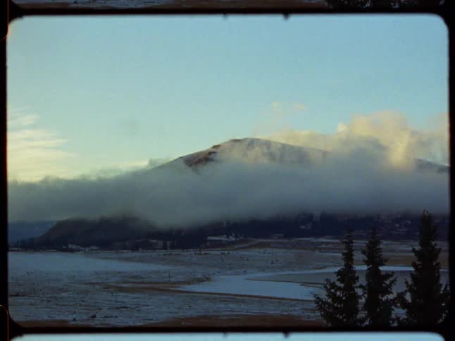Vintage 8mm film captures a serene mountain landscape in winter, with a thick blanket of fog wrapped around the peaks