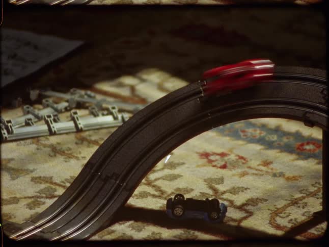 Vintage-style footage shows toy race cars speeding around a track on a sunlit carpet