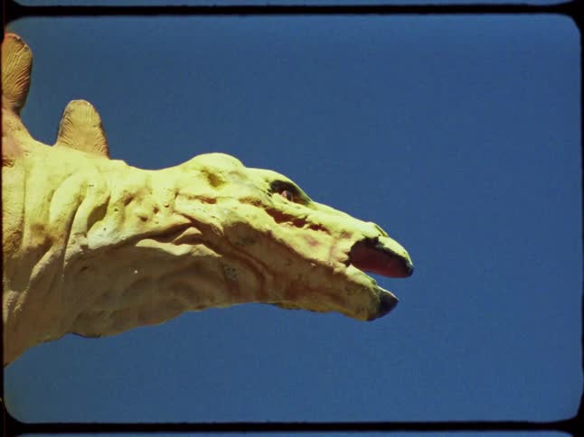 Vintage film zooms into a close-up of a classic Stegosaurus statue at a roadside attraction