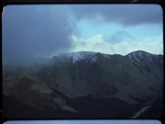 A moody shot of snow-capped mountains partially obscured by fog and stormy clouds