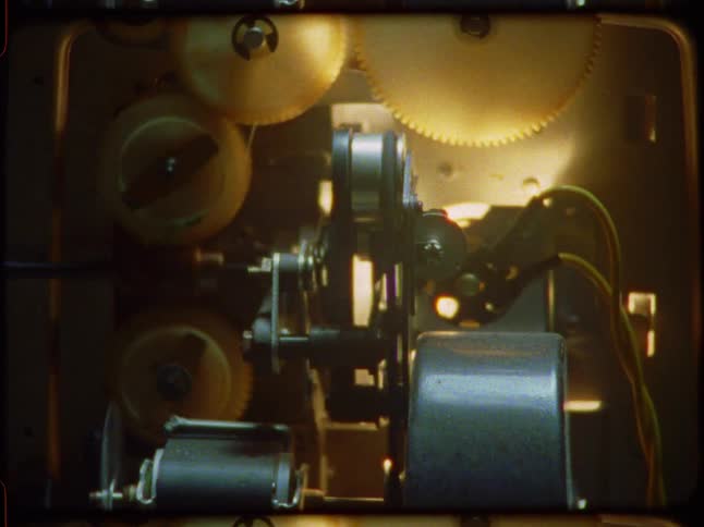 The intricate internal gears and mechanisms of a vintage film projector turn as the camera slowly zooms in